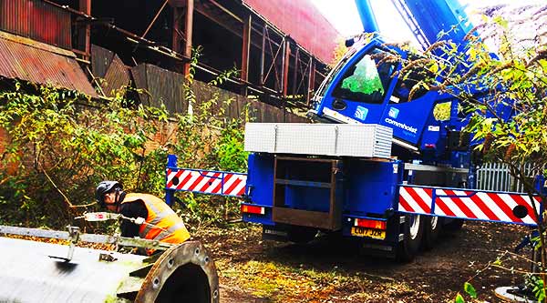 side view of a large metal casting being chained to a crain being lifted on to our scrap mans pick up vehicle