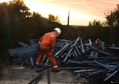 close up view of a howarth scrap metal comany expert dressed in high visibility obright orange water proof work wear and white safety helmet removing unwanted scrap metal from a huge pile located out side a factory