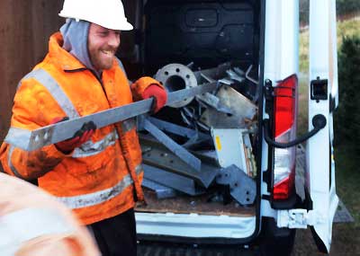 close up view of a scrap team member dressed in bright orange jacket and black waterproof trousers loading a van with scrap metal angle irons