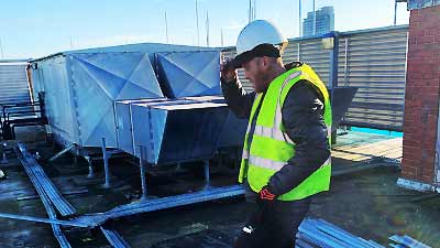 close up side view of a howarths site clearance engineer in site high visibily clothing and a hard hat inspecting some panels that need dismantling on this very large rooftop space