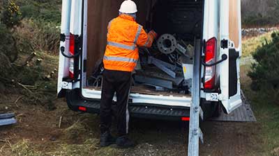 rear photo of a howarth site expert loading unwanted scrap metal items into the back of a white van with both back doors wide open and partially laden with scrap metal