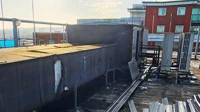 a howarth recycling site clearance expert smartly dressed fully in high visibility clothing completed with the essential white hard hat surveying a large commercial building roof top with a view to completely clearing it of all that site unwanted scrap metal air ducting system