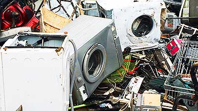 distance view of a large pile of scrap washing machines in various sizes and colours ut mostly white and dented